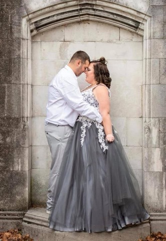 Couple In Formal Attire Embraces Against A Stone Backdrop, Highlighting Their Romantic Connection, Perfect For A Wedding Or Engagement Theme.