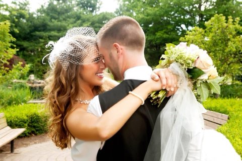 Bride And Groom Embrace Joyfully In A Lush Garden, Showcasing Love And Intimacy On Their Wedding Day With Floral Bouquet And Elegant Attire.