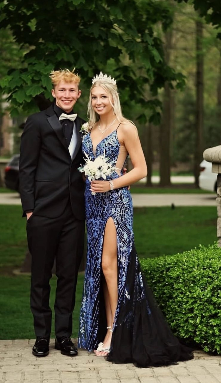 A Young Couple Poses Together, Dressed Elegantly For A Formal Event. The Girl Wears A Blue Gown With A High Slit And A Tiara, While The Boy Is In A Classic Black Suit.